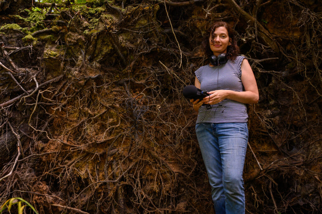 Environmental portrait of Nikki Lindt standing in front of the root system of a large fallen tree at Hubbard Brook taken during her science communication project.